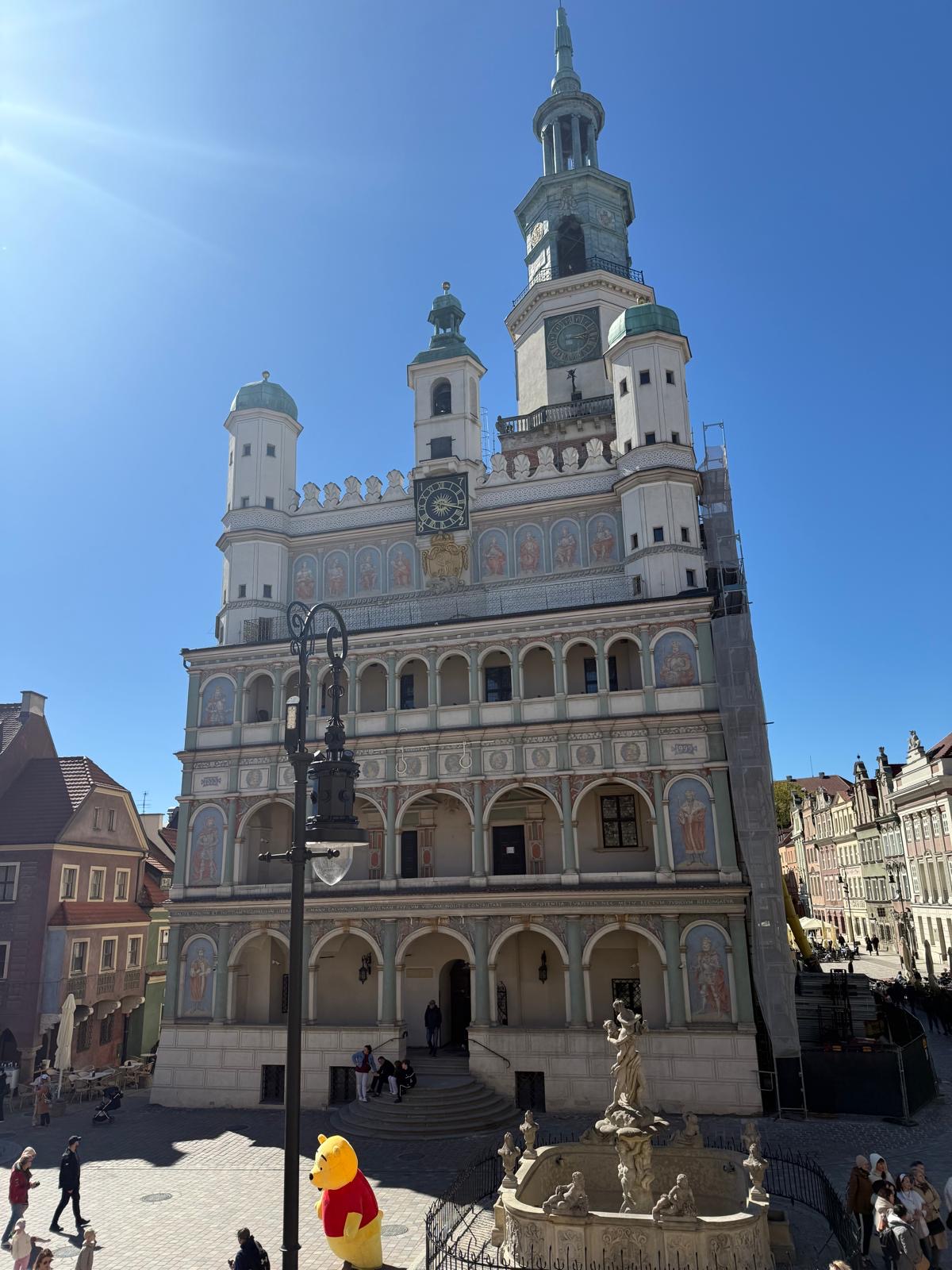 Renesansowy Ratusz na poznańskim Starym Rynku w pełnym słońcu, przed nim fontanna