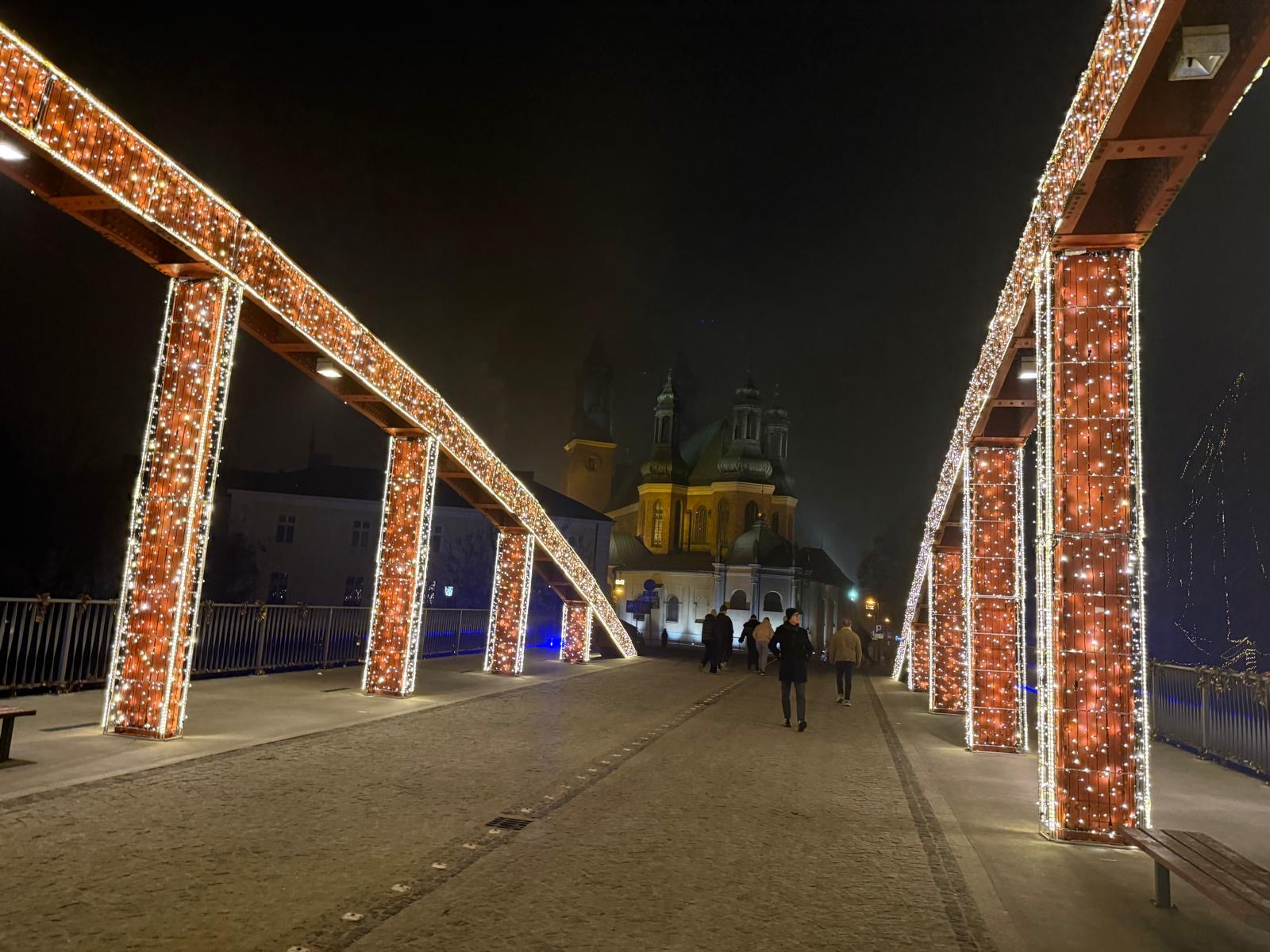 Rozświetlony iluminacją most nad Wartą, w tle podświetlona katedra